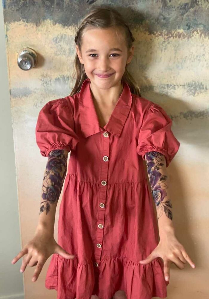 A smiling girl in a red dress with spray-on tattoos on her arms, brightening her day in the hospital.