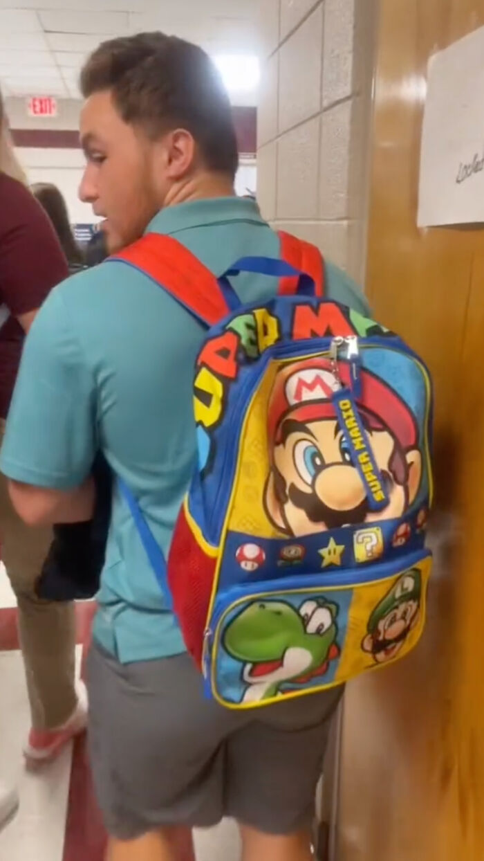 High school senior wearing a colorful Mario-themed kindergarten backpack in a school hallway. High school senior wearing a colorful Mario-themed kindergarten backpack in a school hallway.