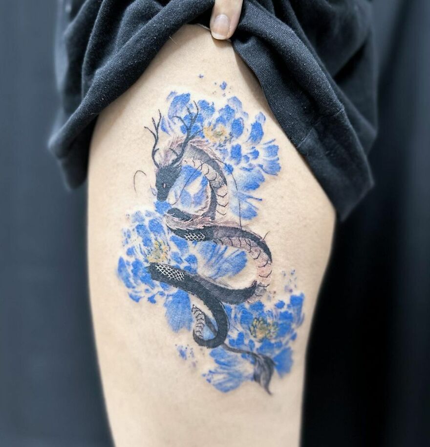 a horned haku dragon tattoo with blue floral decorations
