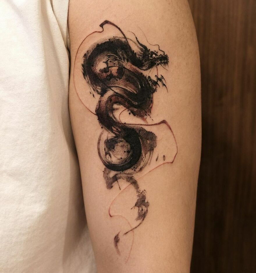 brushstroke style small tattoo of a dragon on biceps 