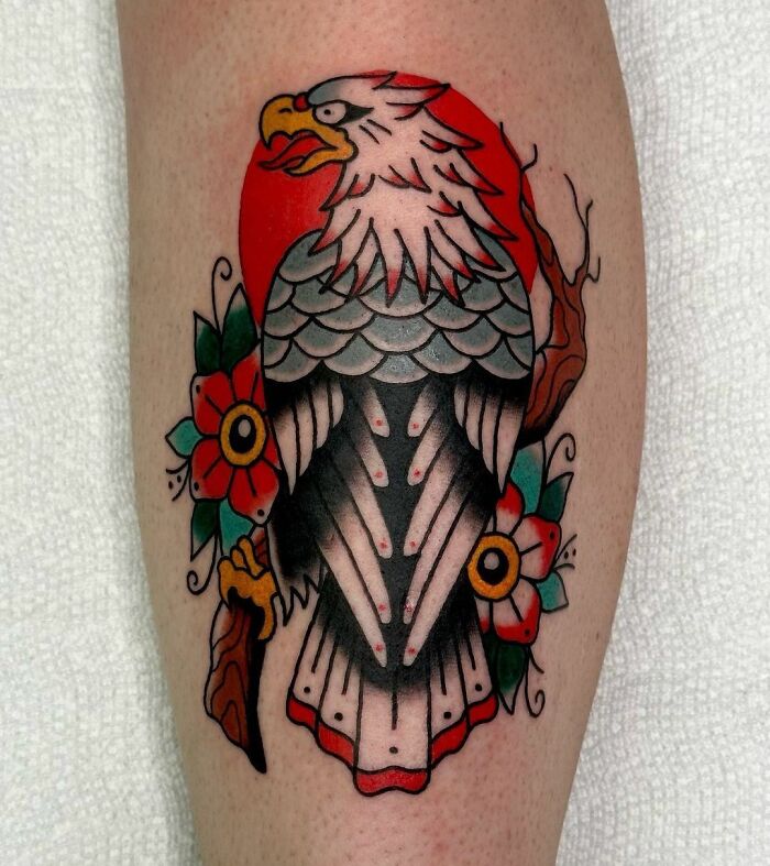 American traditional tattoo of an eagle with flowers and a red sun on skin.