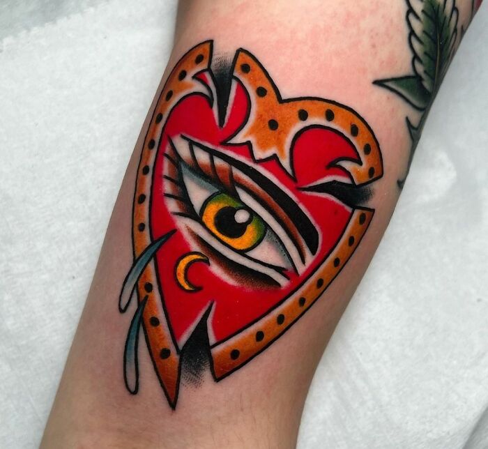 American traditional tattoo design featuring an eye within a red and orange heart on a person's arm.