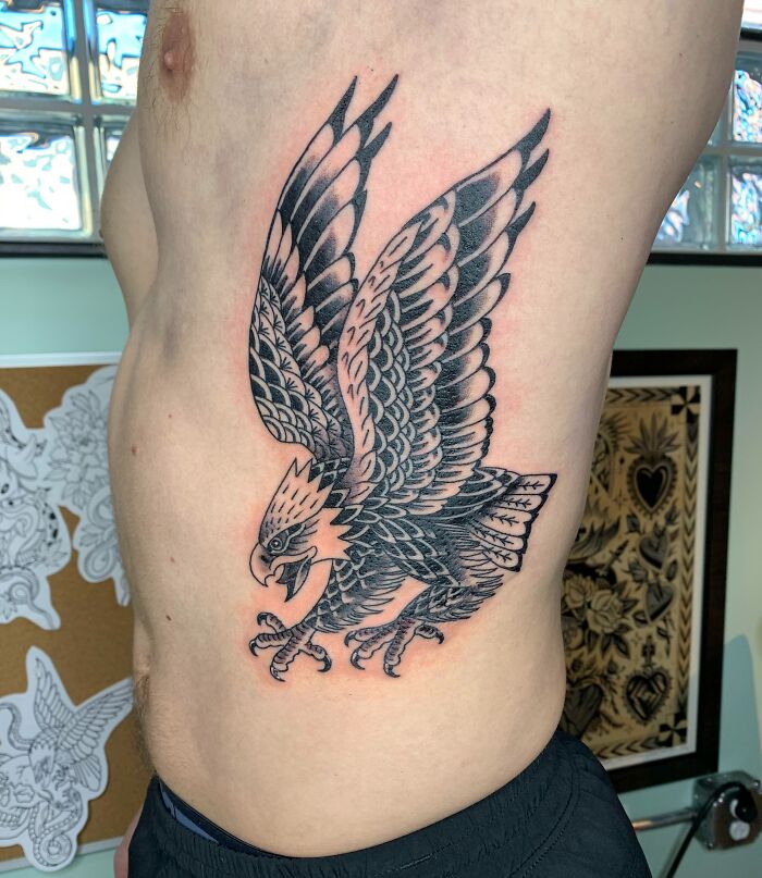 American traditional tattoo of a detailed black and grey eagle on a person's side.