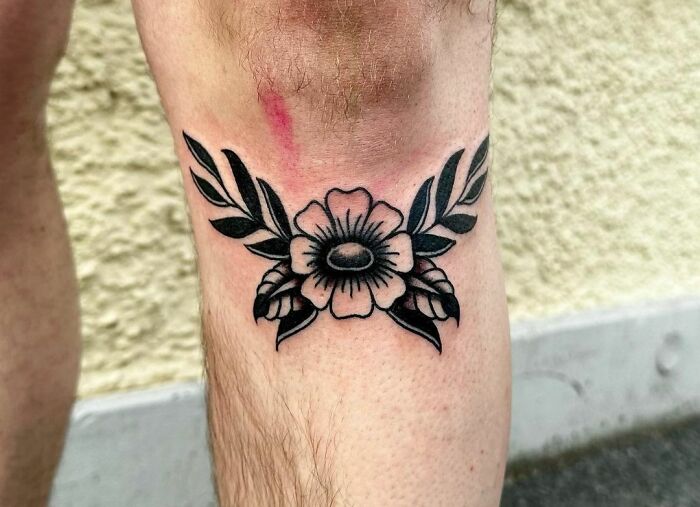 American traditional tattoo with floral and leaf design on a person's knee.