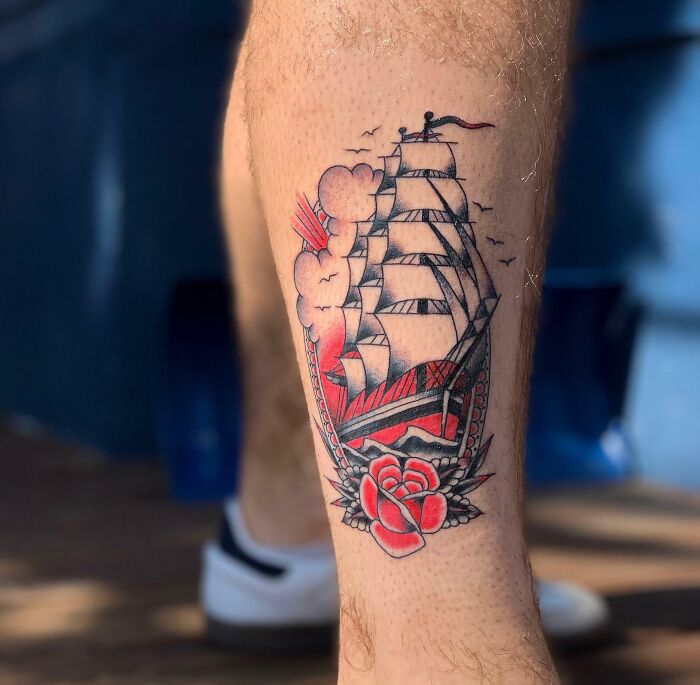 Tattoo of a traditional American ship with red rose details, making a bold statement on a person's leg.