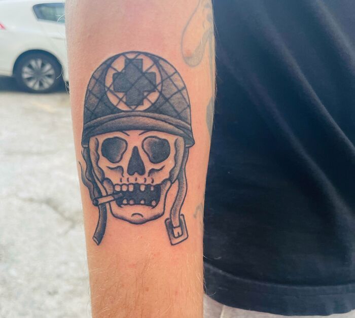 American traditional tattoo of a skull wearing a helmet, inked on a forearm.