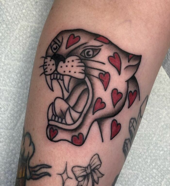 American traditional tattoo of a panther adorned with red heart designs on skin.