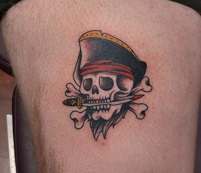 American traditional tattoo featuring a pirate skull with a dagger in its mouth, showcasing bold colors and classic design.