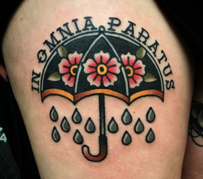 American traditional tattoo of an umbrella with flowers and raindrops, featuring the phrase "In Omnia Paratus."