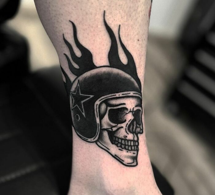 American traditional tattoo of a skull with a flaming helmet and star design on the arm.