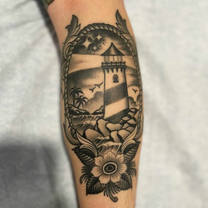 American traditional tattoo of a lighthouse in classic black and gray design, featuring a floral border.