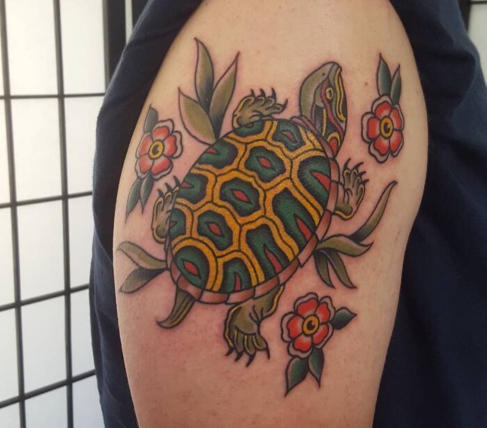 Colorful American traditional turtle tattoo design with flowers on an arm.