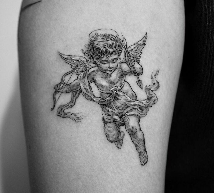 Gothic tattoo of a cherubic angel with wings and a halo on a person's arm.