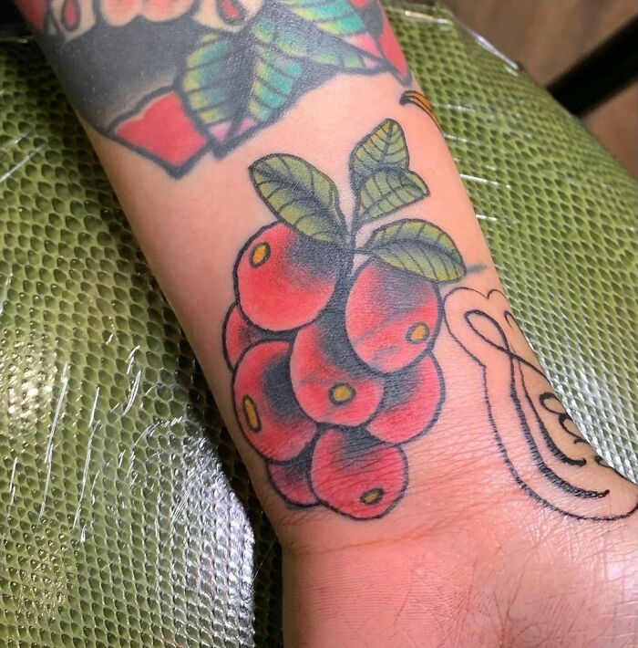 American traditional tattoo design of red cherries with green leaves on an arm.