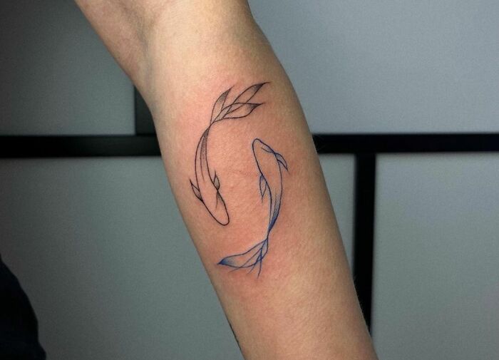 Minimalist Pisces zodiac tattoo on forearm, featuring two abstract fish designs in black and blue line art.