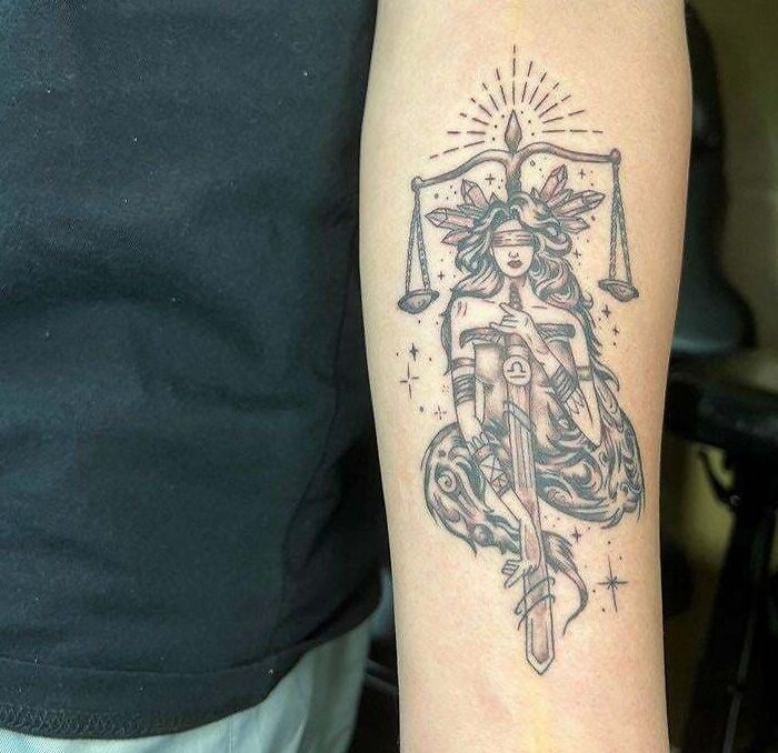 Detailed zodiac tattoo of Libra with scales and sword on forearm.