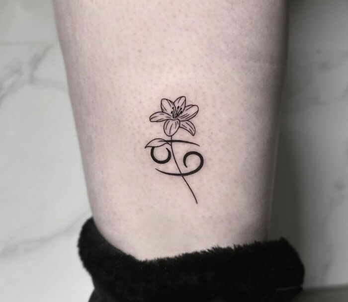Tattoo of a zodiac symbol with a flower, illustrating a creative zodiac tattoo design on a person's leg.