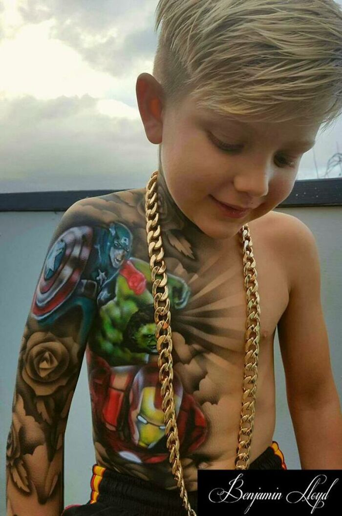 Child smiles with colorful spray-on tattoos featuring superheroes on the arm and chest.