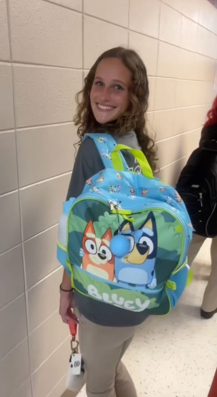 High school senior with a Bluey-themed kindergarten backpack, smiling in a school hallway. High school senior with a Bluey-themed kindergarten backpack, smiling in a school hallway.