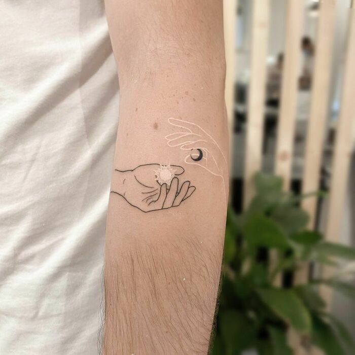 Hands holding moon and sun tattoo 