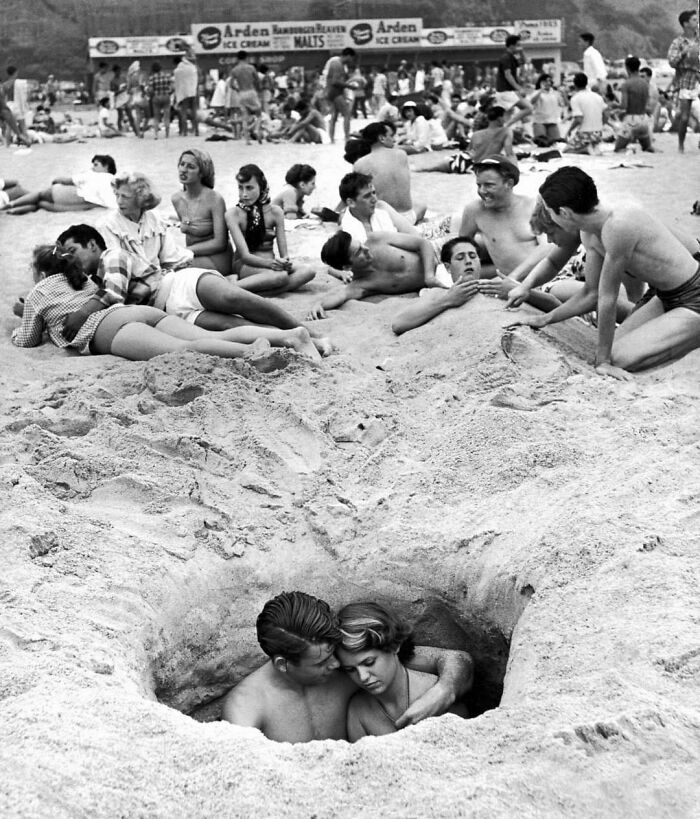 Pareja acurrucada en un agujero mientras los demás disfrutan de la playa durante el 4 de Julio en Santa Mónica, California, 1950 (Foto de Ralph Crane)