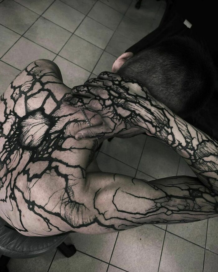 Person with intricate gothic tattoos covering their back and arms, forming a web-like pattern.