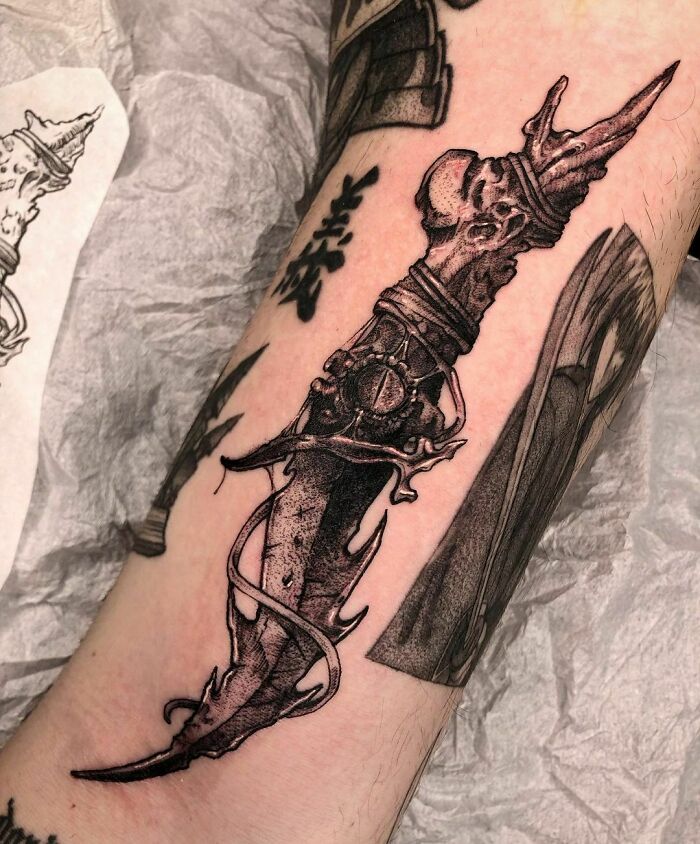 Gothic tattoo of a detailed ornamental dagger on an arm, featuring intricate dark elements and shading.