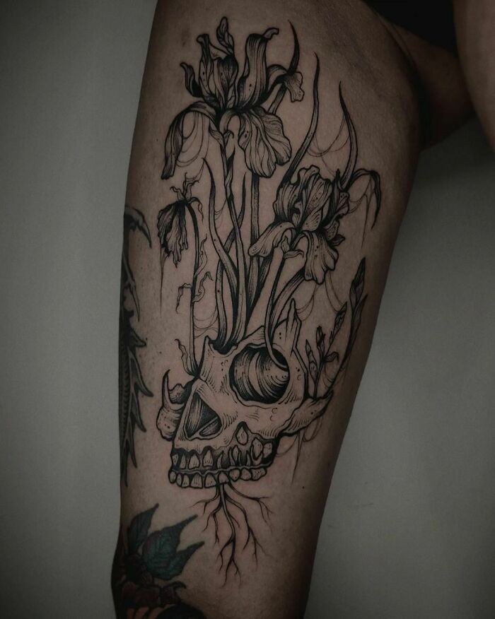 Gothic tattoo of a skull with blooming flowers on a person's arm.