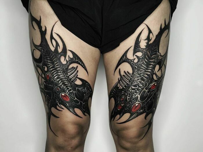 Gothic tattoos depicting dark, intricate designs with red accents on thighs.