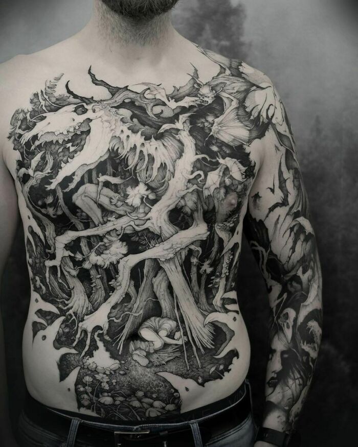Man with a large Gothic tattoo on his chest, featuring intricate mythical creatures and forest elements.