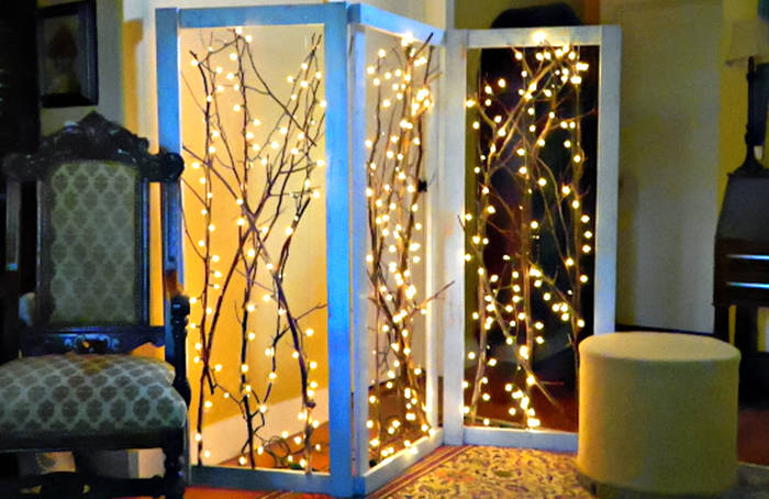 DIY room divider consisting of three wooden white painted frames with tree branches and warm fairy lights inside of them