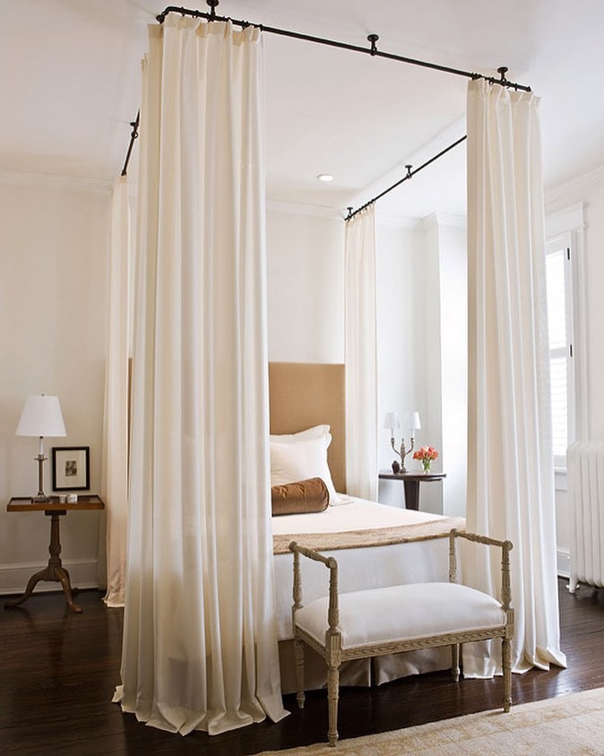 Large beige ceiling-to-floor curtains that hang around the bed and puddle up on the floor