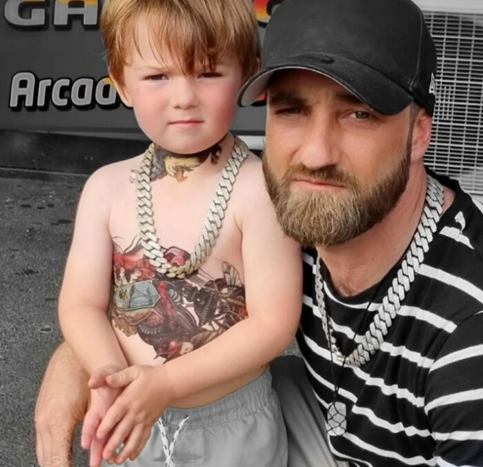 Artist with child showing spray-on tattoos, wearing chain necklaces, enhancing kids' hospital stays.