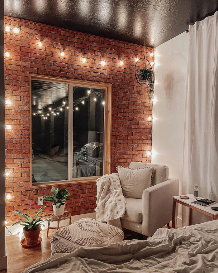 Bedroom with red brick walls, small lights and an armchair in the corner next to bed