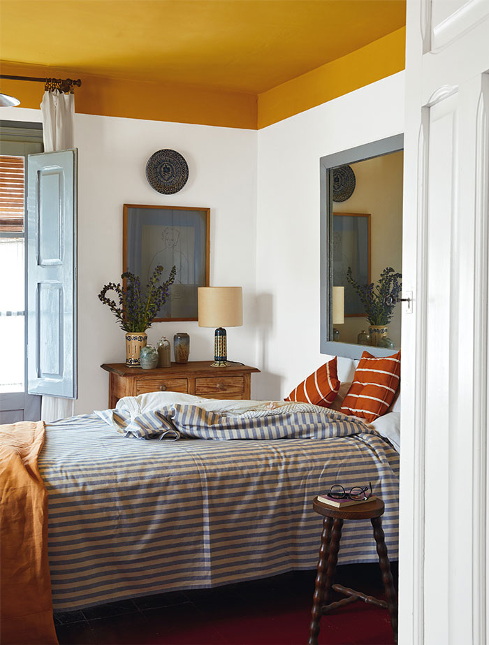 Bright room with yellow ceiling and stripped orange and blue bedding