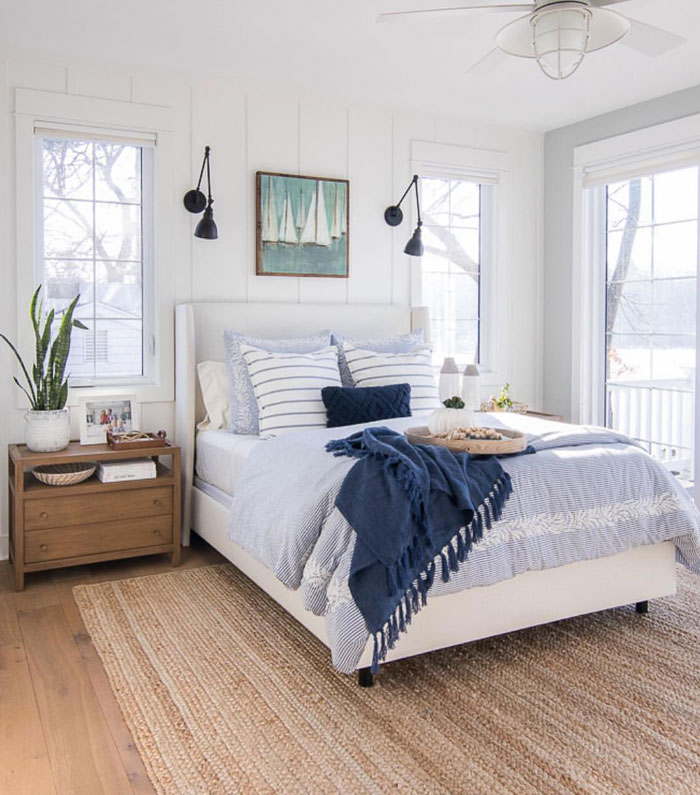 Coastal bedroom with light blue bedding, white walls and picture of boats on it