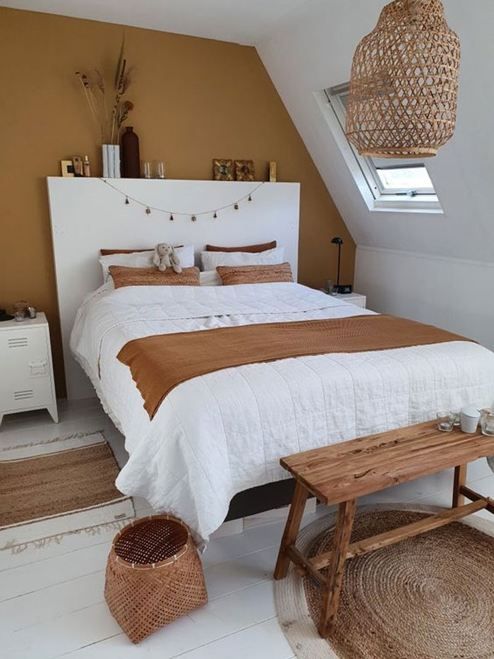 Cozy bedroom with ochre and white colored walls, wooden bench at the foot of the bed, and ochre blanket on the bed