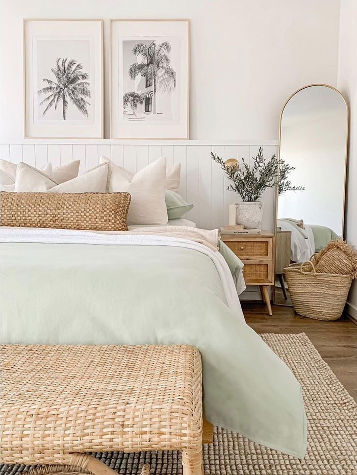 Bright bedroom with white walls and 2 pictures of palms, wooden furniture and mirror in the corner