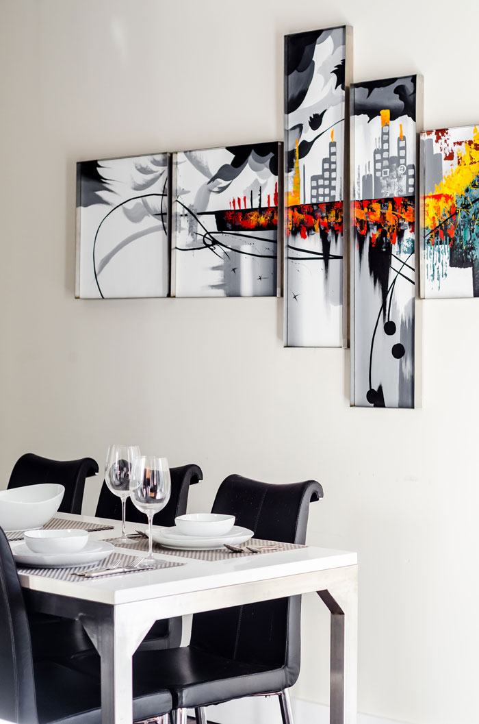 A white and black breakfast nook with five vibrant pieces of art on the wall behind it
