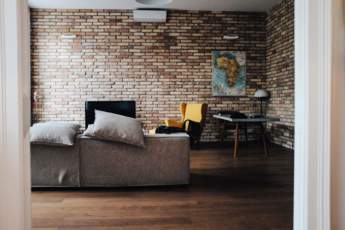 Rustic bricks wall in a room with gray couch and gray wooden table beside wing chair