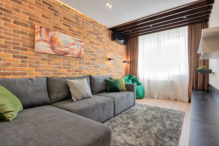 Gray sectional couch with throw pillows and rustic brick wall