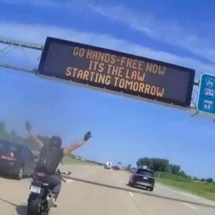 Motorcyclist riding hands-free on highway beneath sign about new hands-free law, related to images venturing beyond internet.