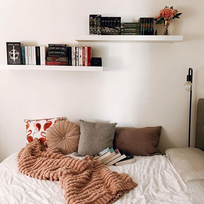 Bookshelf on wall with books and bed with white sheets and pillows