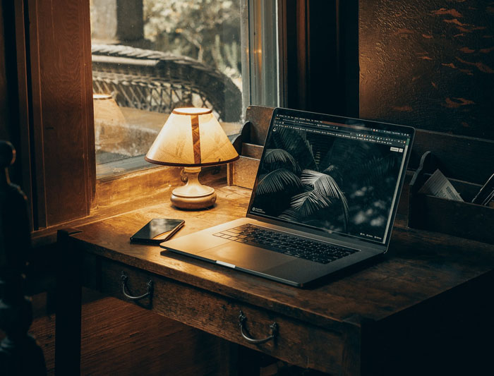 macbook pro on brown wooden table and lighted lamp