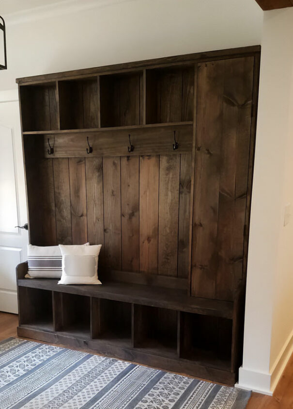 A hall tree made with dark brown distressed wood with two pillows placed on the bench A hall tree made with dark brown distressed wood with two pillows placed on the bench