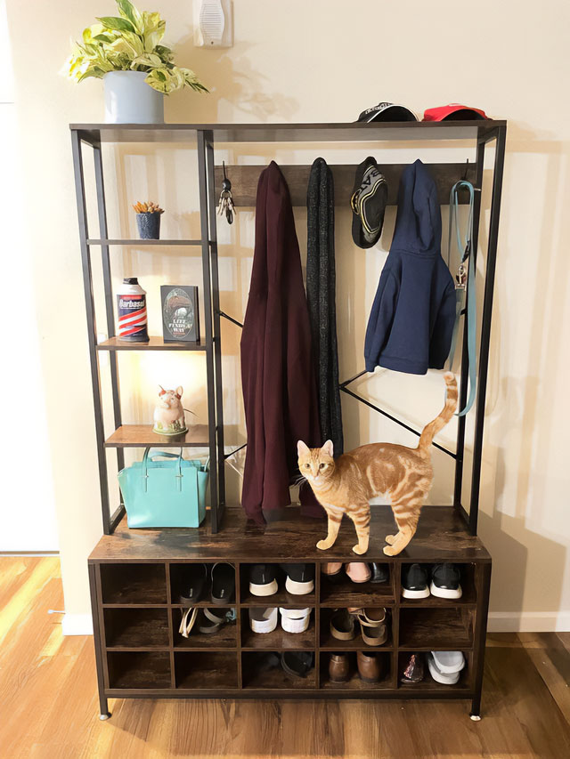 A metal and wooden hall tree with many items, ample shoe storage space, and an orange cat standing on it