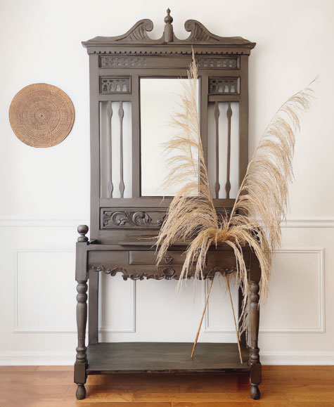 A wooden hall tree with a mirror and two feathers on it A wooden hall tree with a mirror and two feathers on it