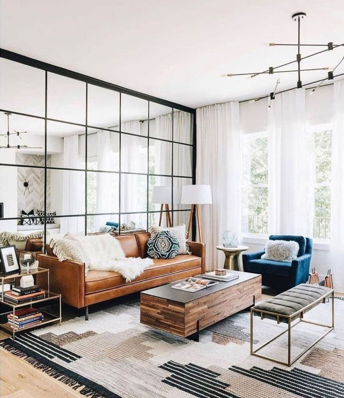 Living room with a mirror over the entire wall, brown leather couch and coffee table