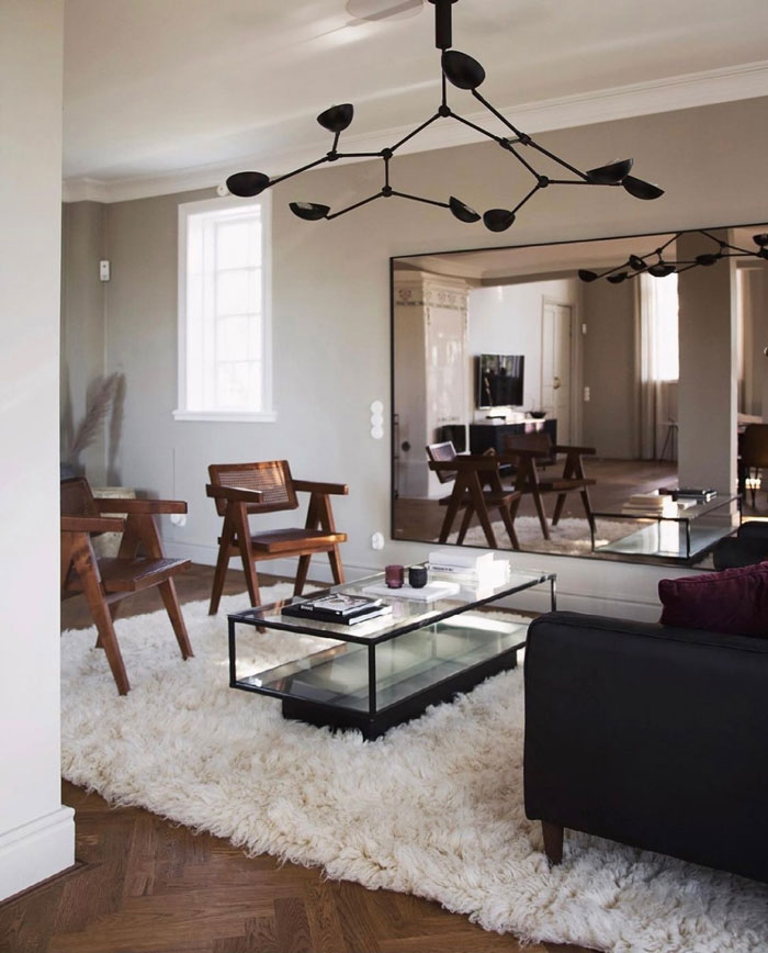 Living room ideas featuring a black chandelier, large wall mirror, wooden chairs, and a cozy white rug in a modern interior. Living room ideas featuring a black chandelier, large wall mirror, wooden chairs, and a cozy white rug in a modern interior.