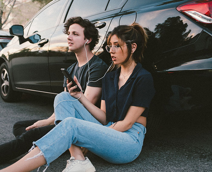 Woman and man sitting near car and listening music